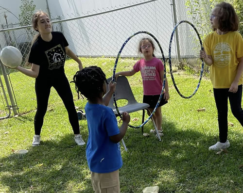 A teacher and students throwing a volley ball through hula hoops.