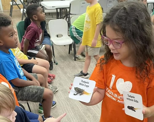 A girl student showing her classmates a picture of a tadpole with legs.
