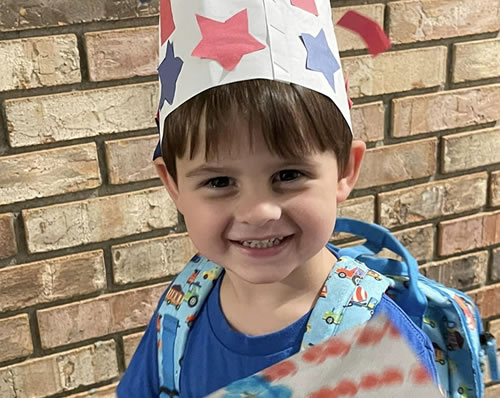 K-3 student dressed showing off his fourth of July hat and picture he drew.